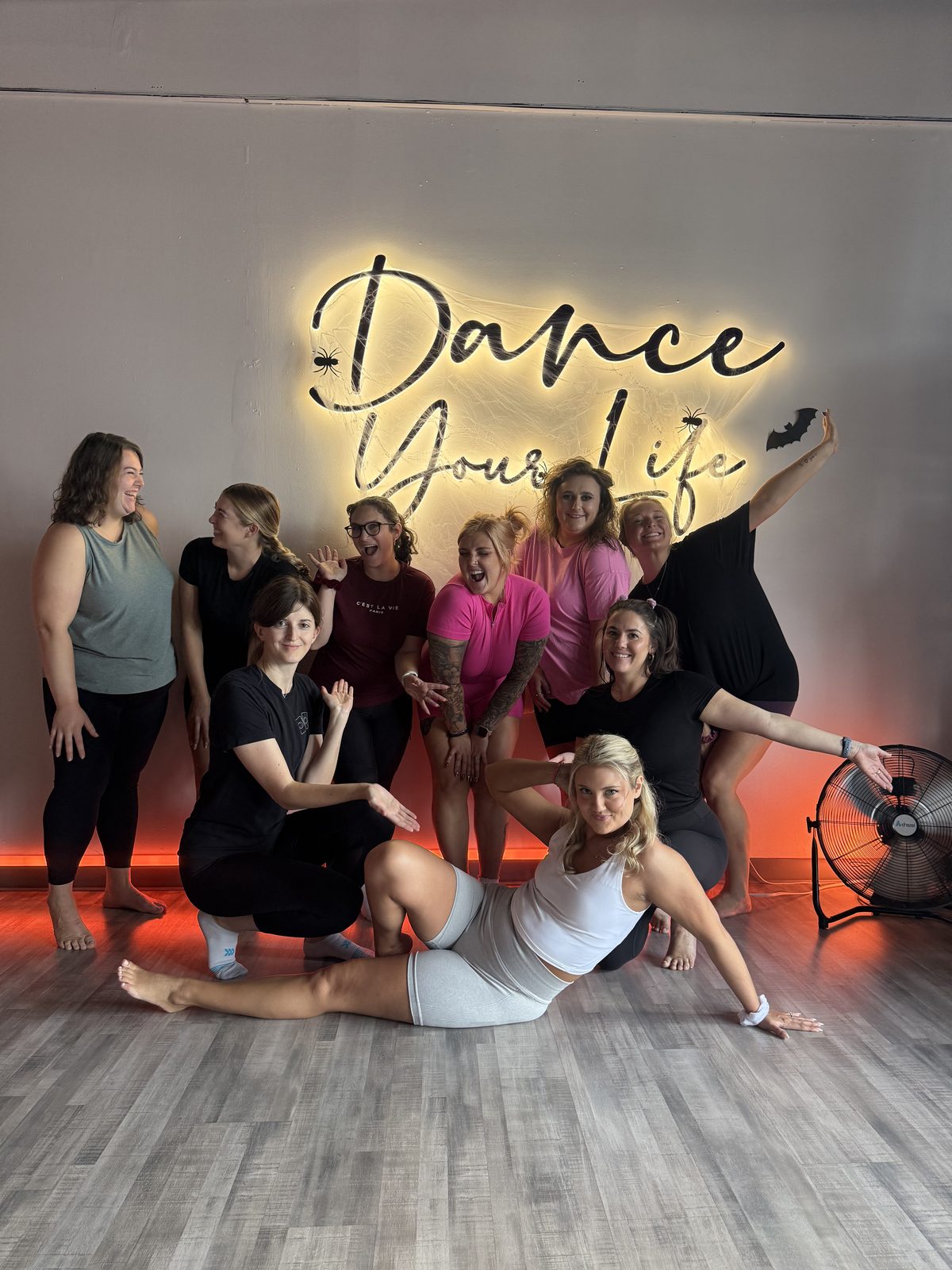 Bridesmaids and the bride striking playful poses in front of the Dance Your Life neon sign during their private bachelorette party